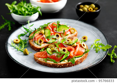 Toasts with salted salmon, arugula, green olives and cucumber 95766833