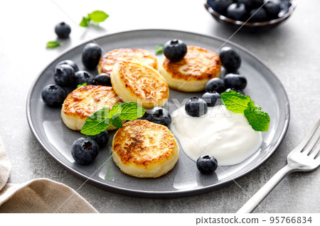 Cottage cheese fritters with fresh blueberry and yogurt for breakfast 95766834