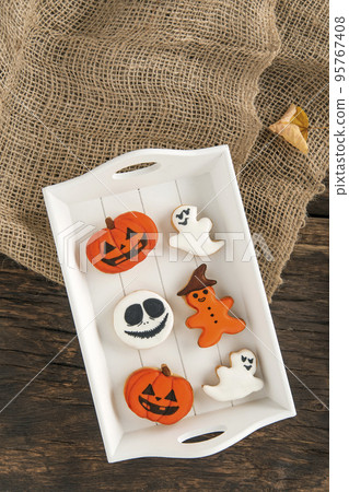 Orange gingerbread in pumpkin shape and ghosts. Halloween sweets lie in a wooden tray. Tasty cookie on table. Top view 95767408
