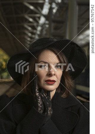Portrait of middle-aged aristocratic woman in black wide-brimmed hat with veil and lace gloves. 95767542
