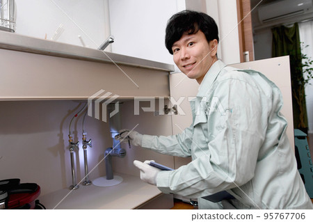 A man in work clothes checking under the sink 95767706