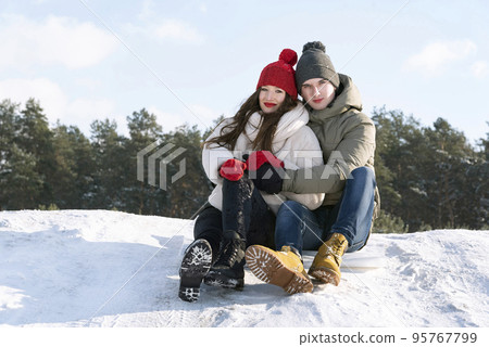 Teenagers sit and hug against the background of a winter forest and blue sky. Date in nature 95767799