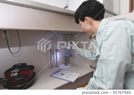 A man in work clothes checking under the sink 95767980