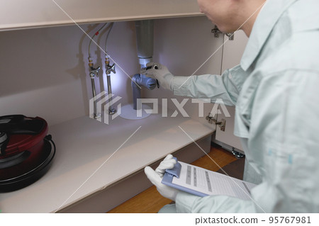 一個穿著工作服的男人在水槽下檢查 95767981