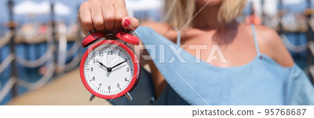 Smiling female tourist holding an alarm clock on sea pier 95768687
