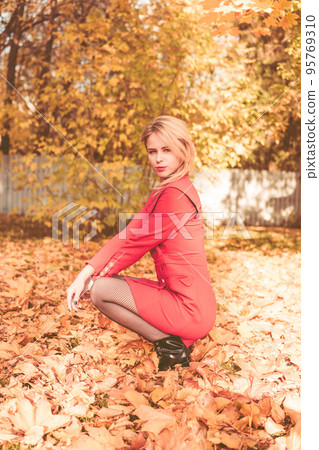 Portrait of a blonde next to a red-orange bush in autumn. The concept of the autumn season 95769310