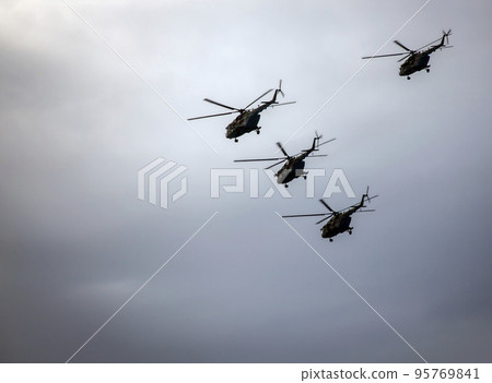 Four military helicopters are flying in battle formation in dark stormy sky. Four military helicopters are flying in battle formation in dark stormy sky. 95769841