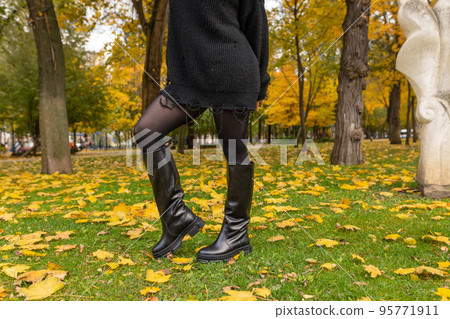A girl in warm boots poses against a background of fallen foliage 95771911