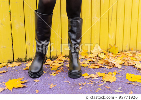 A girl in warm boots poses against a background of fallen foliage 95771920