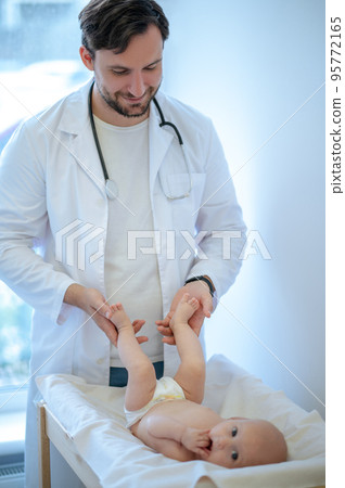 Dark-haired surgeon checking babys legs and smiling to a baby 95772165
