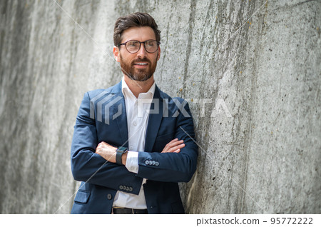 An elegant young man in eyeglasses standing near the wall An elegant young man in eyeglasses standing near the wall 95772222