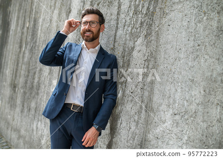 An elegant young man in eyeglasses standing near the wall An elegant young man in eyeglasses standing near the wall 95772223