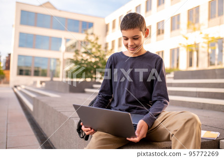 Joyous adolescent using his portable computer outdoors Joyous adolescent using his portable computer outdoors 95772269
