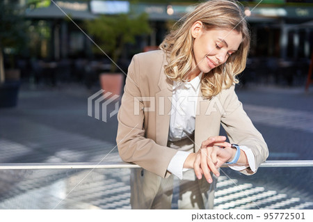 Portrait of corporate woman checks her time, stands on street outside office and looks at her wrist watch 95772501