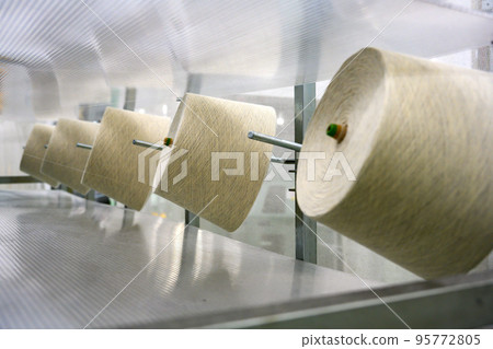 Threads on bobbins waiting to be woven in a bright spinning mill 95772805