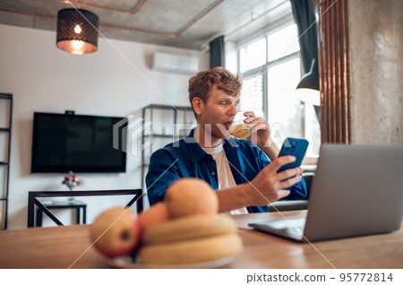 A happy man sitting at the table in the home office and working A happy man sitting at the table in the home office and working 95772814