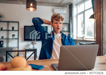 Ginger man reading something onlines and looking shocked Ginger man reading something onlines and looking shocked 95772826