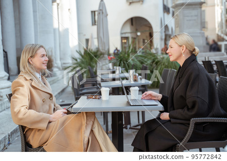 Two blonde women discussing plans for future trip in a street cafe Two blonde women discussing plans for future trip in a street cafe 95772842