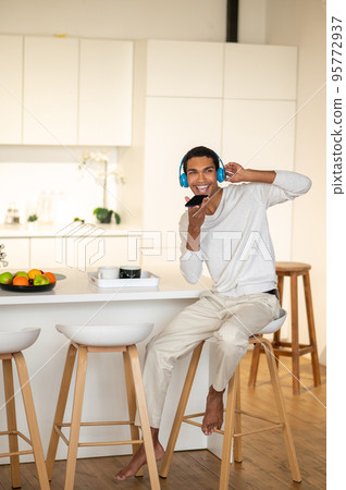 Young dark-skinned man in headphones listening to music and looking excited Young dark-skinned man in headphones listening to music and looking excited 95772937