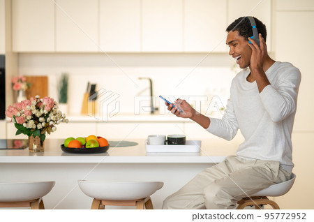 Young man sitting in the kitchen and listening to music in headphones 95772952