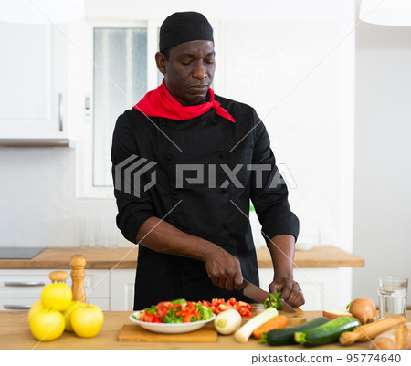 Proffesional male cook in black uniform chopping vegetables 95774640