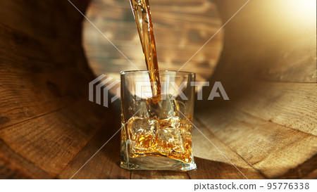 Pouring whisky into glass inside old wooden barrel. Pouring whisky into glass inside old wooden barrel. 95776338