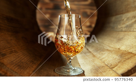 Pouring rum into glass inside old wooden barrel. Pouring rum into glass inside old wooden barrel. 95776340