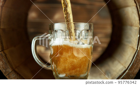 Pouring beer into glass inside old wooden barrel. 95776342