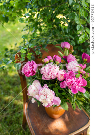 Pink peony in a jug on an old vintage wooden chair, rustic still life. A bouquet for a wedding or birthday. 95778418