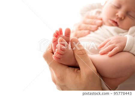 Top view of a newborn girl lying in a white overalls in the arms of her parents. Beautiful portrait of a little girl with closed eyes. The hands of the parents gently hug the child's body. 95778443