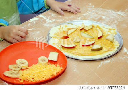 child in uniform preparing fruit pizza closeup 95778624