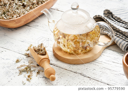 Glass tea kettle of herbal Icelandic moss tea. Wooden scoop and bowl of dried Iceland moss. Cetraria islandica - latin name of plant. Alternative herbal medicine. 95779590