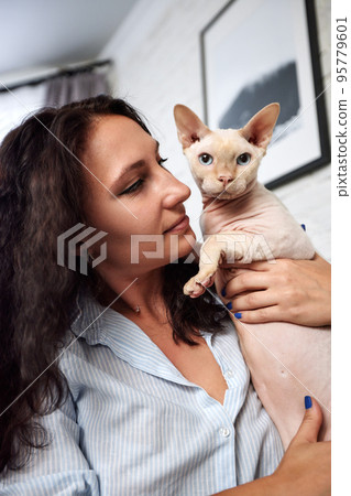 Portrait of young woman holding cute cat with blue eyes. Female hugging her cute short hair kitty. Background, copy space, close up. Adorable domestic pet concept. 95779601