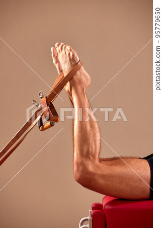 Fit man doing a lunge stretch yoga pilates exercise to strengthen and tone his muscles using a reformer in a gym 95779650