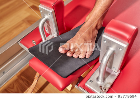 Fit man doing a lunge stretch yoga pilates exercise to strengthen and tone his muscles using a reformer in a gym 95779694