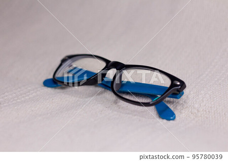 Eyeglasses with a black frame and blue temples close-up on a light background. Eyeglasses with a black frame and blue temples close-up on a light background. 95780039