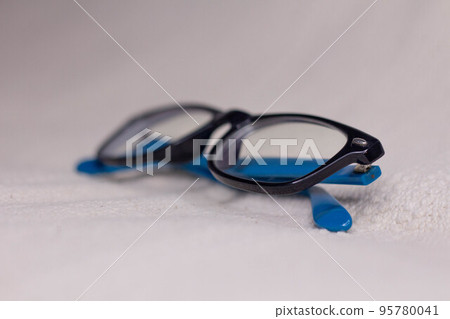 Eyeglasses with a black frame and blue temples close-up on a light background. 95780041
