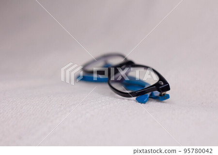 Eyeglasses with a black frame and blue temples close-up on a light background. 95780042