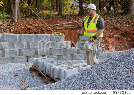 Building retaining wall with retaining blocks on new property is being done by construction worker Building retaining wall with retaining blocks on new property is being done by construction worker 95780363