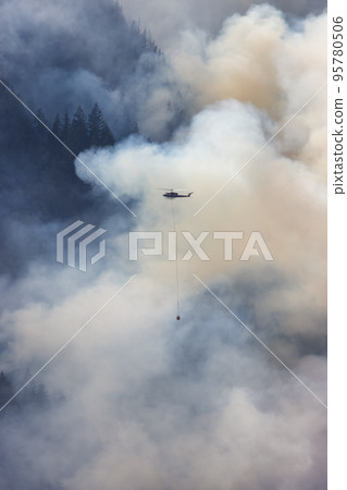 Wildfire Service Helicopter flying over BC Forest Fire and Smoke on the mountain near Hope 95780506