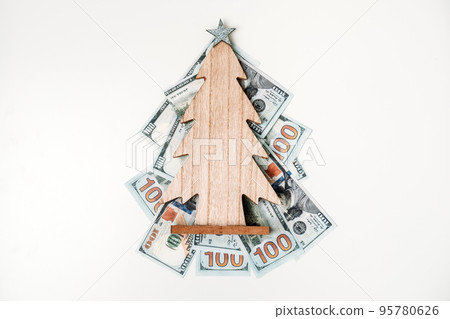 How To Spend, Christmas budget and saving concept. wooden Christmas tree on Stack of dollar bills on white table How To Spend, Christmas budget and saving concept. wooden Christmas tree on Stack of dollar bills on white table 95780626