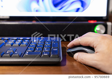 Selective focus on a hand that is clicking on a mouse with monitor and soundbar out of focus in background. 95780669