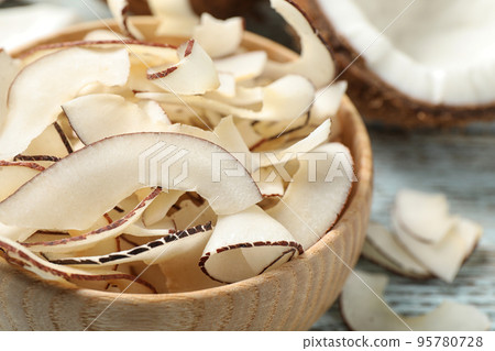 Tasty coconut chips in wooden bowl, closeup Tasty coconut chips in wooden bowl, closeup 95780728