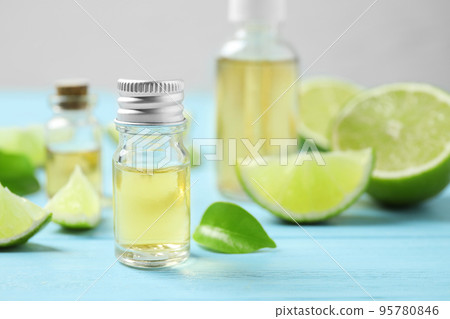 Lime essential oil and cut citrus fruits on light blue wooden table. Space for text 95780846