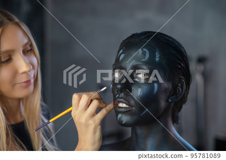 Woman applies creative makeup to the face of a nice young model 95781089