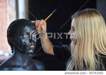 Woman applies creative makeup to the face of a lovely young model 95781091