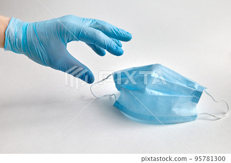 A person in a blue protective glove reaches for a protective medical mask. Means of antiviral and antibacterial protection A person in a blue protective glove reaches for a protective medical mask. Means of antiviral and antibacterial protection 95781300