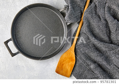 Black cast iron empty frying pan, wooden spatula and gray kitche Black cast iron empty frying pan, wooden spatula and gray kitche 95781301