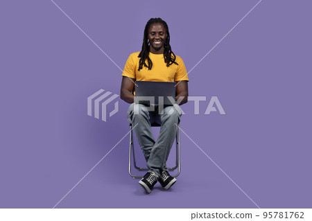 Positive black man sitting on chair, using laptop Positive black man sitting on chair, using laptop 95781762