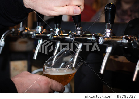 Partially blurred hand pouring beer from silvery bar tap in a pub 95782328